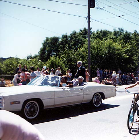 A white Cadillac convertible carrying Ted Knight along the parade route, spectators lining the roadside.