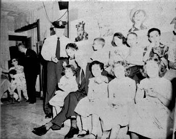 Ted Knight in uniform standing with a studio audience of children seated in rows.